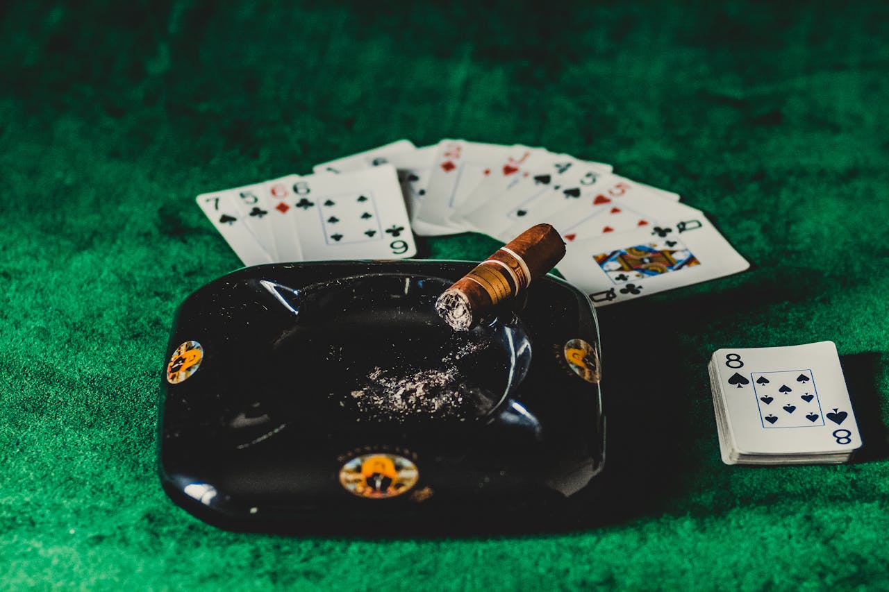 services-03 A poker table with playing cards, a lit cigar, and an ashtray on a green felt surface.