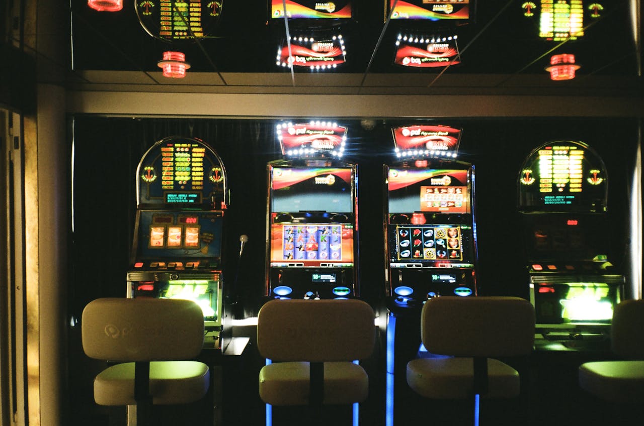 who-we-are Slot machines in a dimly lit casino with reflective ceiling and empty chairs.